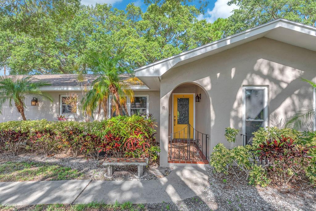 A single-story house exterior features a bright yellow front door, arched entryway, and landscaped yard — 11081 143RD STREET, LARGO, FL