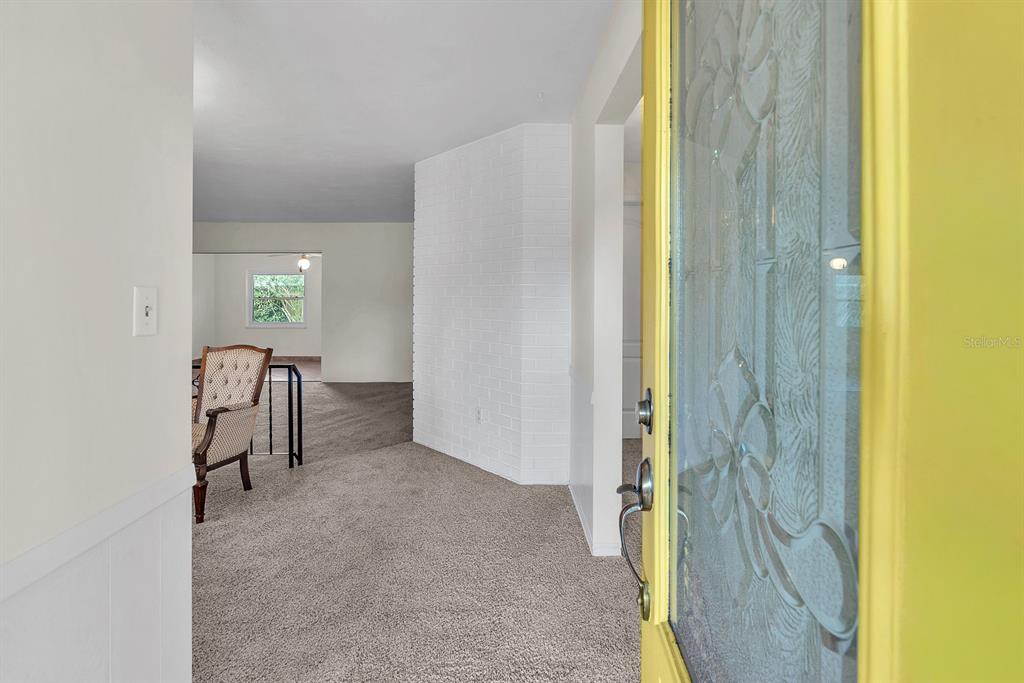 An entryway with carpeted flooring leads to a living area featuring a white brick wall — 11081 143RD STREET, LARGO, FL