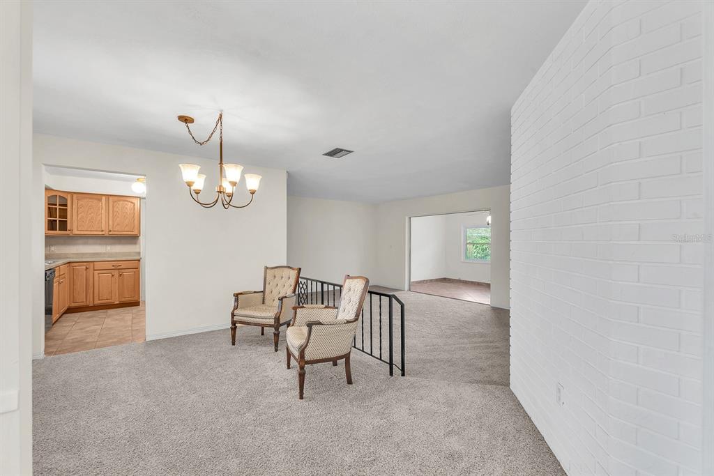 A carpeted dining area features two chairs, a chandelier, and a view into the kitchen — 11081 143RD STREET, LARGO, FL