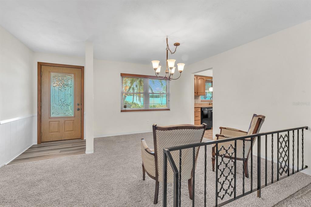 A dining area features a chandelier, carpeted flooring, a front door, and a metal railing — 11081 143RD STREET, LARGO, FL