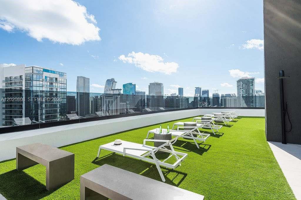 A rooftop terrace features artificial turf, lounge chairs, and a glass railing overlooking a city skyline — 225 N Miami Ave # 2810, Miami FL 33128, MIAMI, FL
