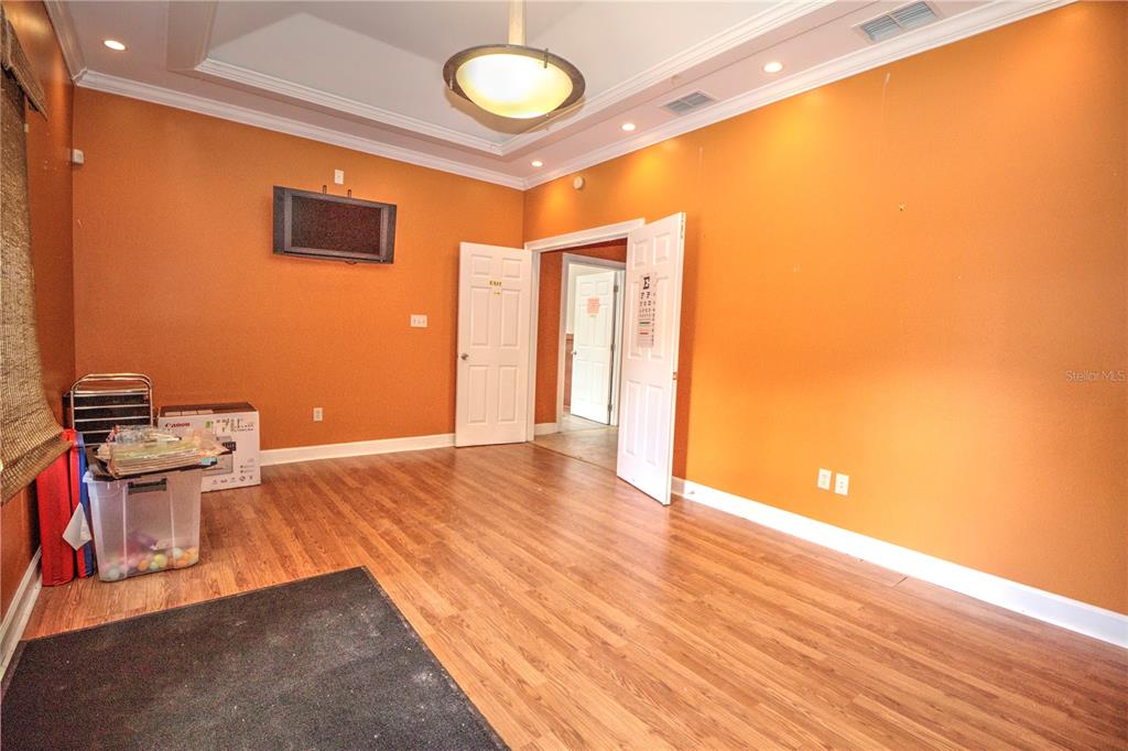 An empty room with orange walls, wood-look flooring, a tray ceiling, and two open doors — 2131 SW 22ND PLACE UNIT 100, OCALA, FL