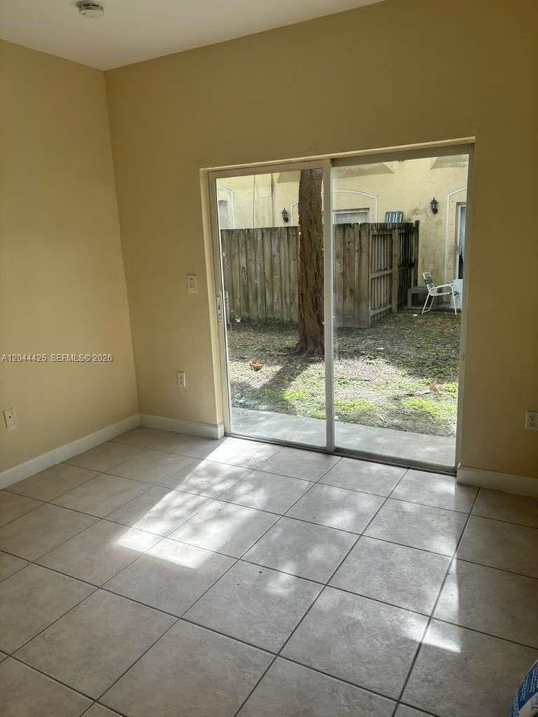 A room with light-colored tile flooring and a sliding glass door leading to a yard — 1663 SE 27th Dr # 207, Homestead FL 33035, HOMESTEAD, FL