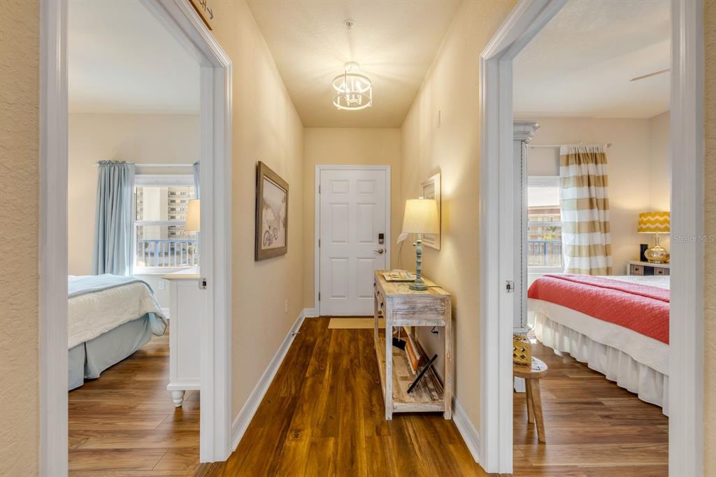 A hallway with wood-look flooring leads to a white door between two bedrooms — 5300 S ATLANTIC AVENUE UNIT 19-504, NEW SMYRNA BEACH, FL