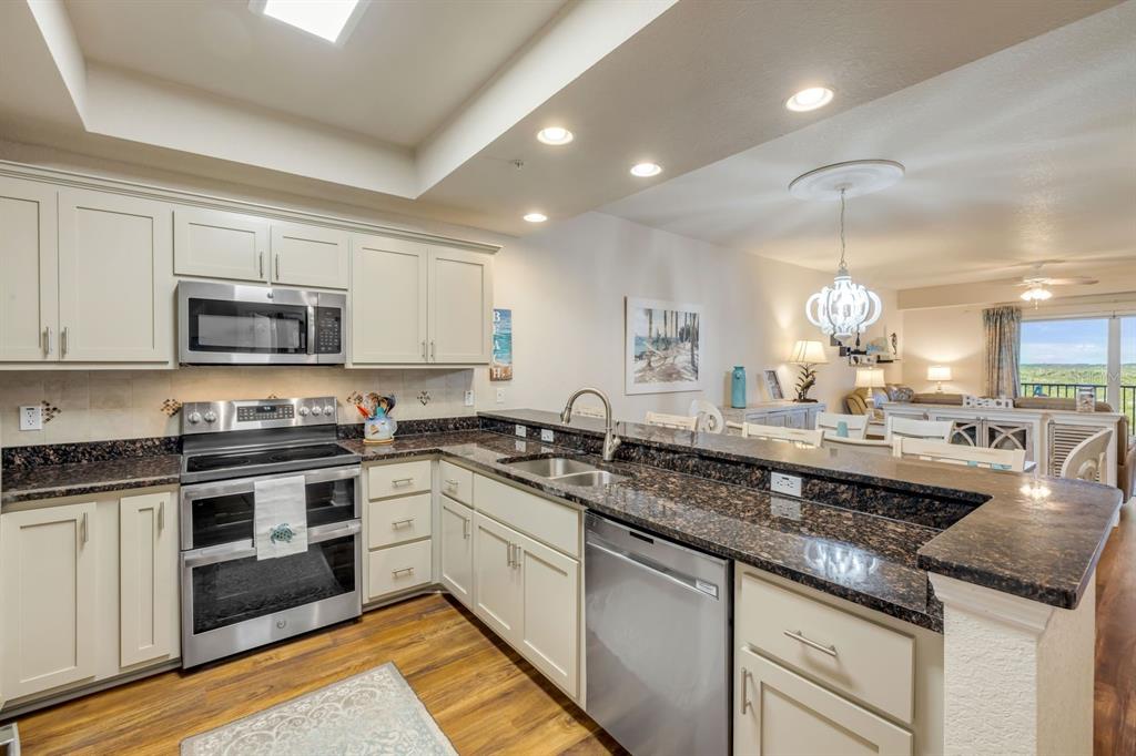 A kitchen with white cabinets, dark granite countertops, and stainless steel appliances overlooks a living area — 5300 S ATLANTIC AVENUE UNIT 19-504, NEW SMYRNA BEACH, FL