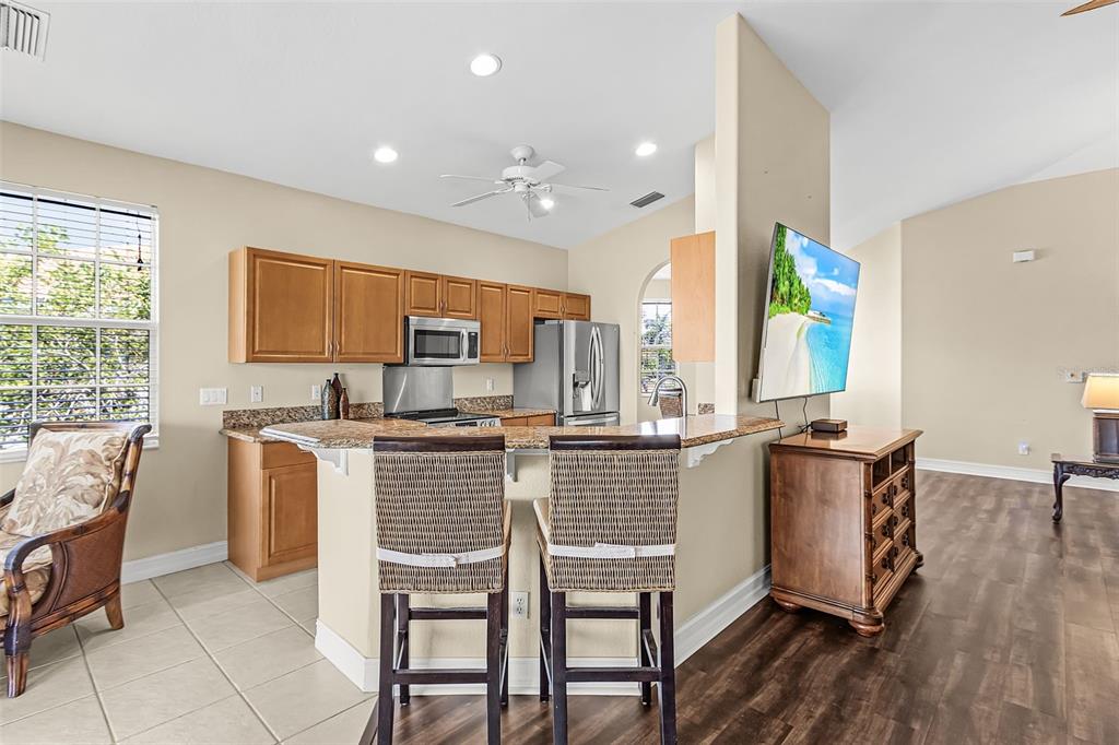 A kitchen with wood cabinets and granite countertops overlooks a living area with a television — 5626 CAPE HARBOUR DRIVE UNIT 202, CAPE CORAL, FL
