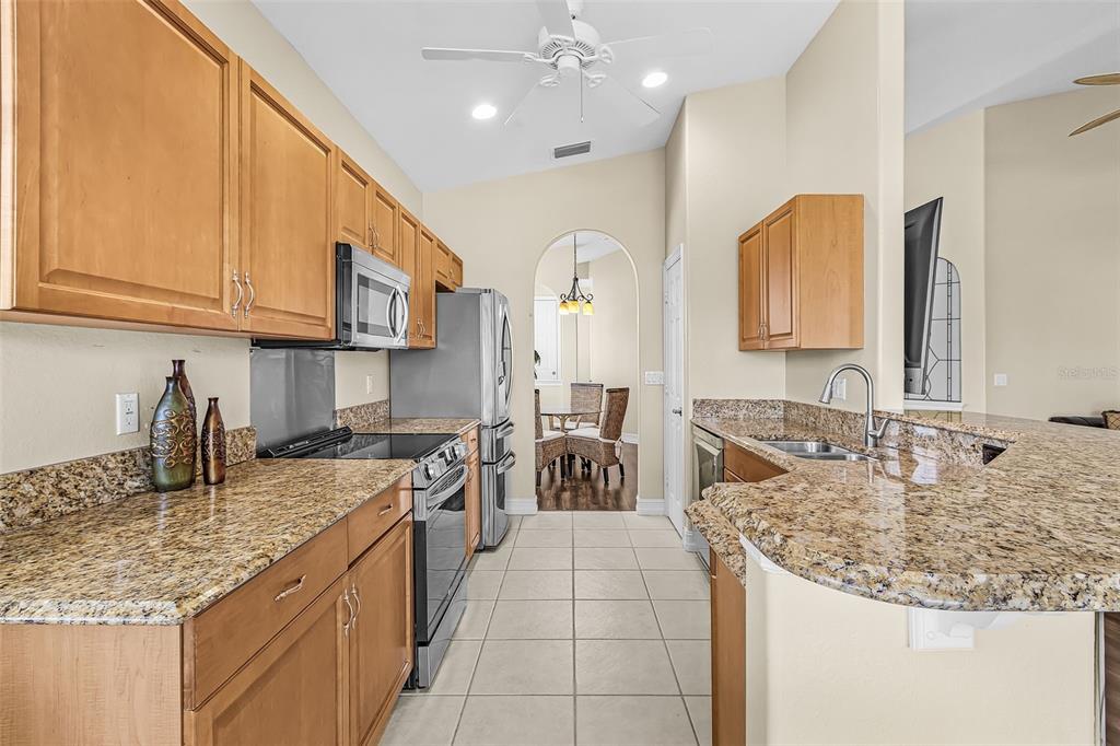A kitchen with light wood cabinets, granite countertops, stainless steel appliances, and tile flooring — 5626 CAPE HARBOUR DRIVE UNIT 202, CAPE CORAL, FL