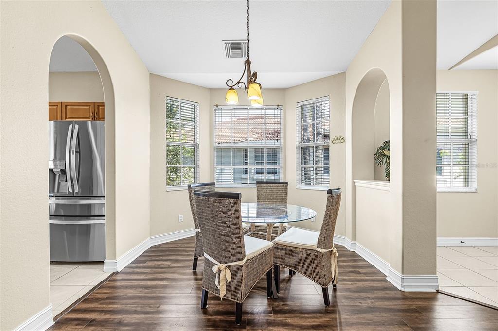 A dining area features a glass table, wicker chairs, wood-look flooring, and arched wall openings — 5626 CAPE HARBOUR DRIVE UNIT 202, CAPE CORAL, FL