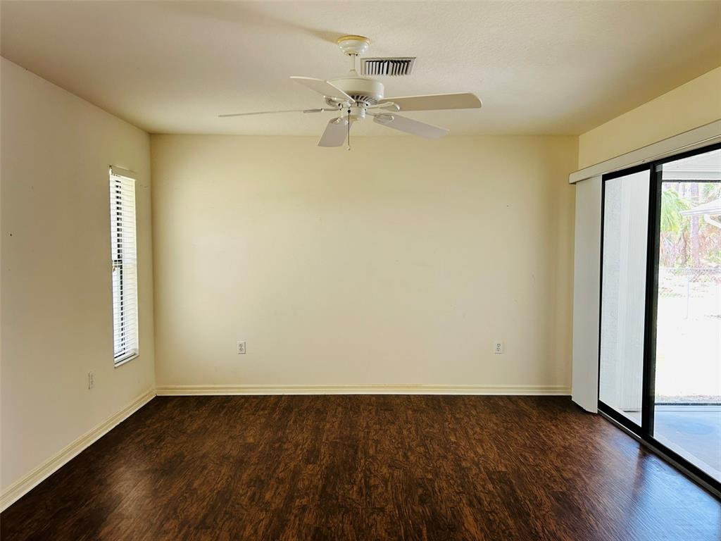 An empty room features dark wood-look flooring, a ceiling fan, and sliding glass patio doors — 304 PINE GLEN COURT, ENGLEWOOD, FL