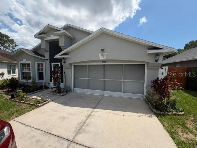 A gray suburban house features a three-car garage and a concrete driveway under a cloudy sky — 4049 SAVAGE STATION CIRCLE, NEW PORT RICHEY, FL