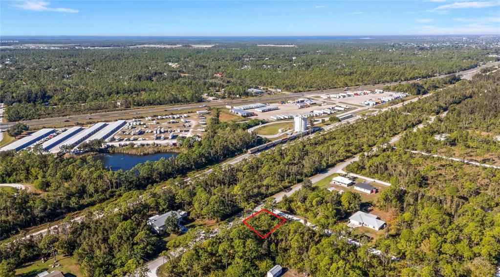 An aerial view shows a wooded lot outlined in red near a highway and industrial area — 12198 BUENOS COURT, PUNTA GORDA, FL