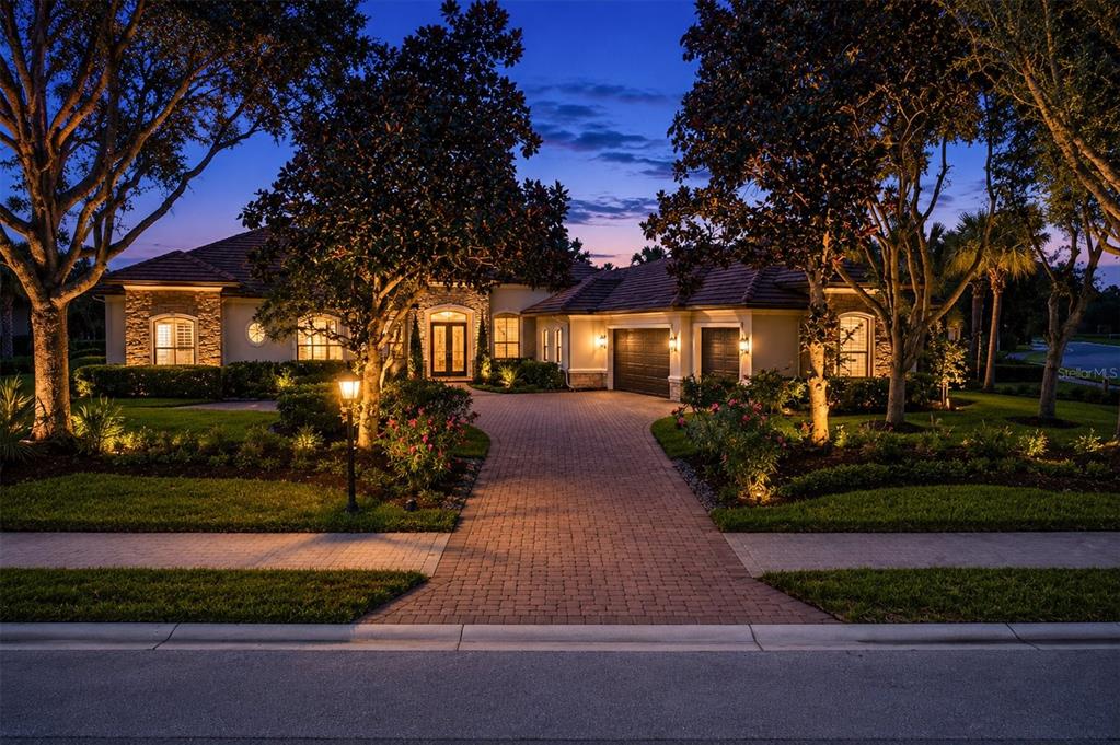 A single-story house with a brick driveway and landscape lighting at dusk — 9261 MCDANIEL LANE, SARASOTA, FL