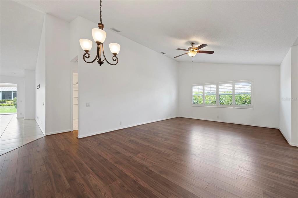 A spacious, empty room features dark wood-look flooring, white walls, a chandelier, and a ceiling fan — 5368 KELLY DRIVE UNIT 17, SARASOTA, FL