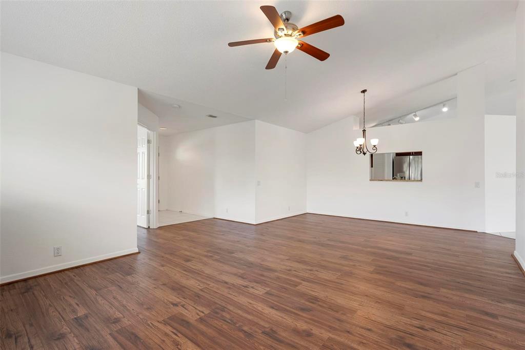 An empty living room with white walls, wood-look flooring, a ceiling fan, and a chandelier — 5368 KELLY DRIVE UNIT 17, SARASOTA, FL