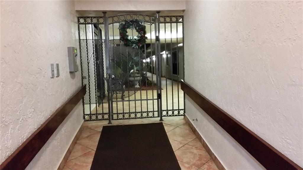 A gated entryway leads to a tiled hallway with wooden handrails on both walls — 1001 BENJAMIN FRANKLIN DRIVE UNIT 506, SARASOTA, FL