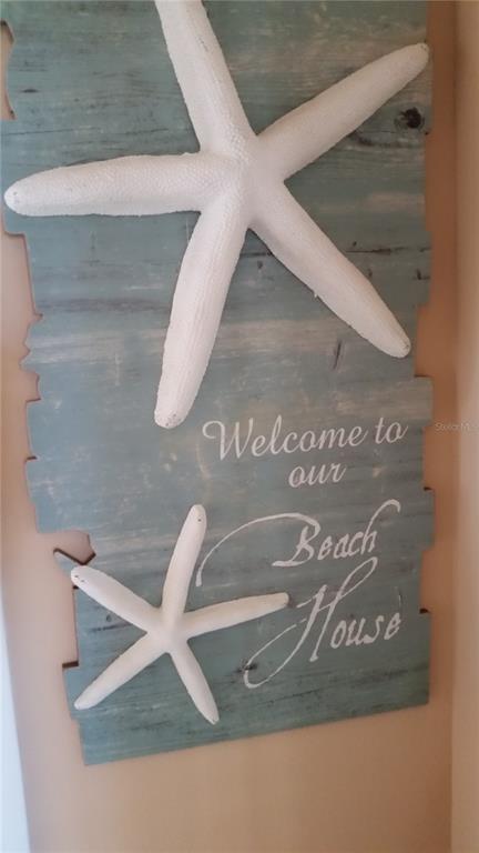 A decorative wooden wall sign features two white starfish and the text Welcome to our Beach House — 1001 BENJAMIN FRANKLIN DRIVE UNIT 506, SARASOTA, FL