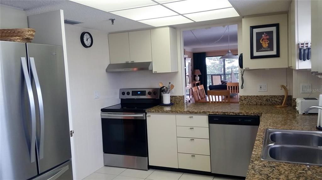 A kitchen features stainless steel appliances, granite countertops, and white cabinets under a drop ceiling — 1001 BENJAMIN FRANKLIN DRIVE UNIT 506, SARASOTA, FL