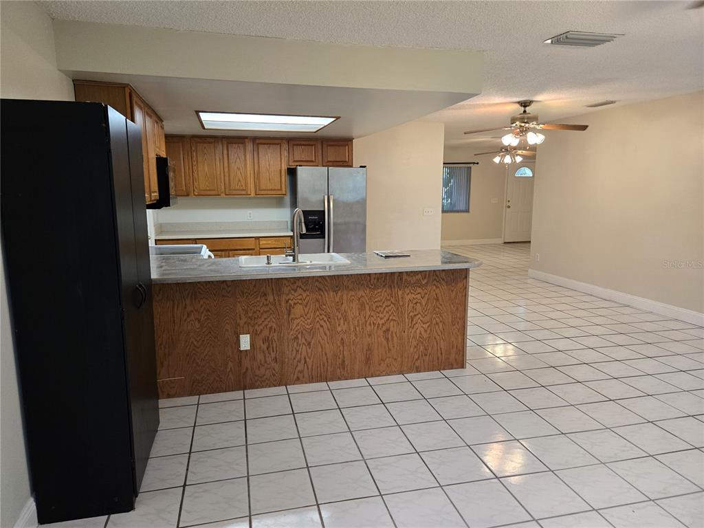 A kitchen with wood cabinets and a breakfast bar overlooks an open tiled living area — 8430 PORT SAID, ORLANDO, FL