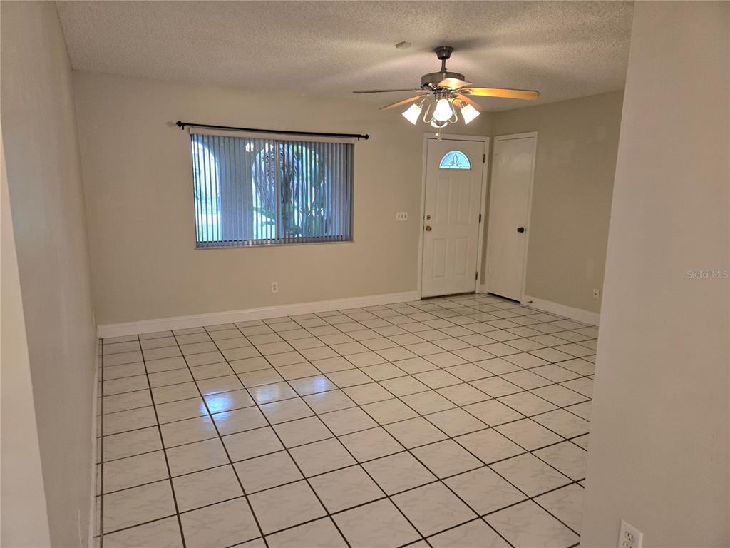 An empty room features white tile flooring, a ceiling fan, and a front entry door — 8430 PORT SAID, ORLANDO, FL