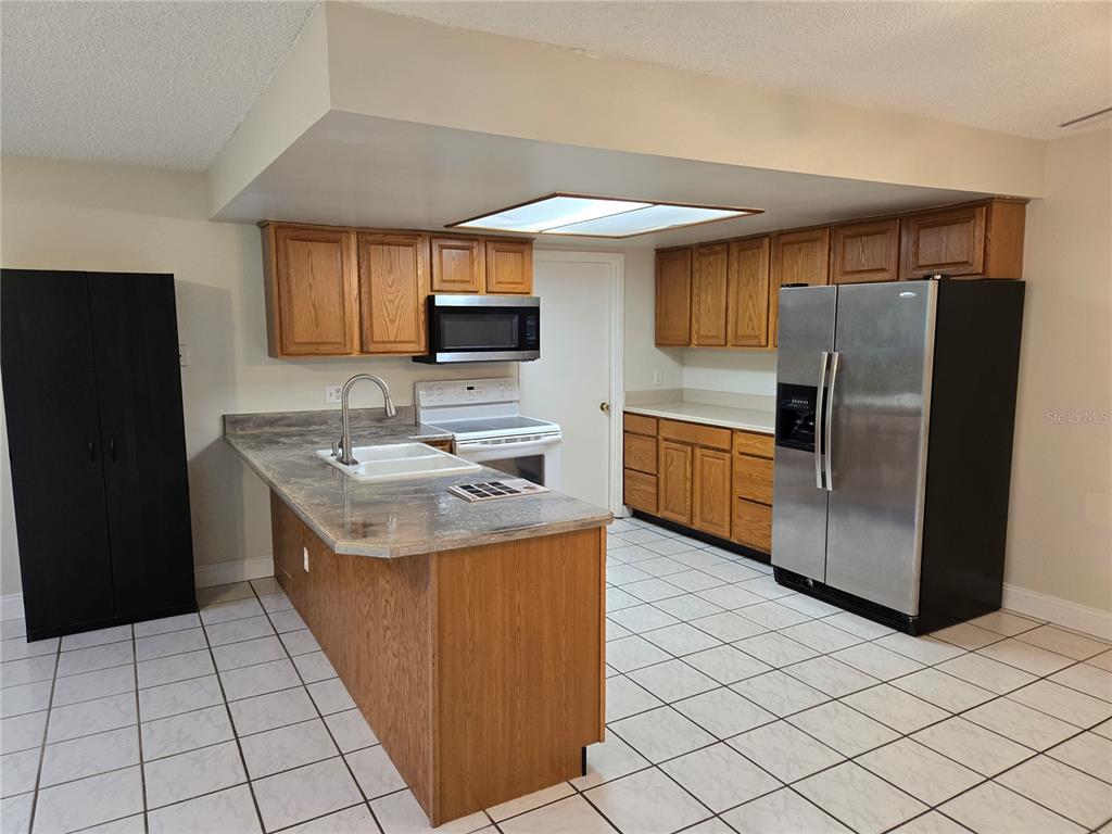 A kitchen features oak cabinets, a laminate countertop, white tile flooring, and stainless steel appliances — 8430 PORT SAID, ORLANDO, FL