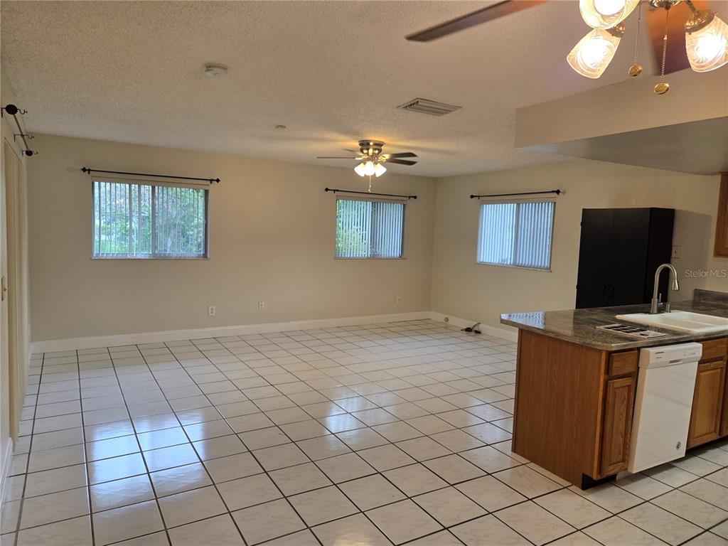 A bright, open-concept living and kitchen area features white tiled floors and beige walls — 8430 PORT SAID, ORLANDO, FL