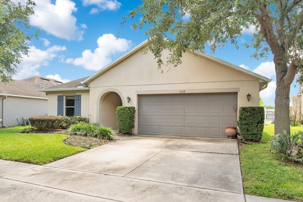 A single-story suburban house with a beige stucco exterior, a two-car garage, and a driveway — 2319 PLANTATION OAK DRIVE, ORLANDO, FL
