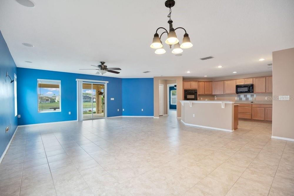 An open-concept living area features blue walls, tile flooring, and an adjacent kitchen with cabinets — 2319 PLANTATION OAK DRIVE, ORLANDO, FL
