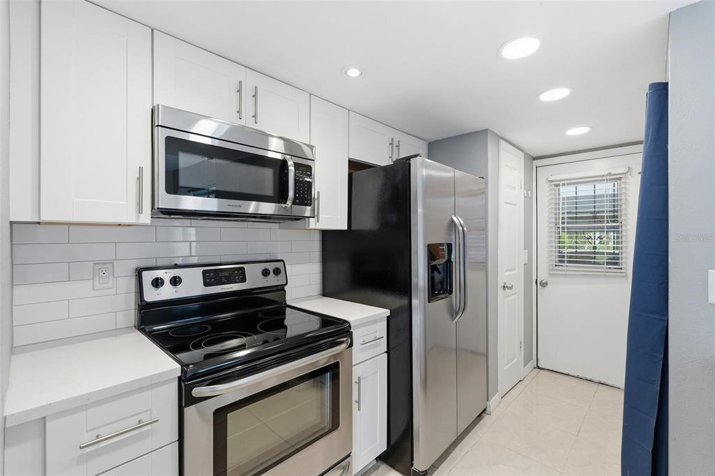 A kitchen features white cabinets, stainless steel appliances, a black stove, and a white door — 6902 EL CENTRO COURT, TAMPA, FL