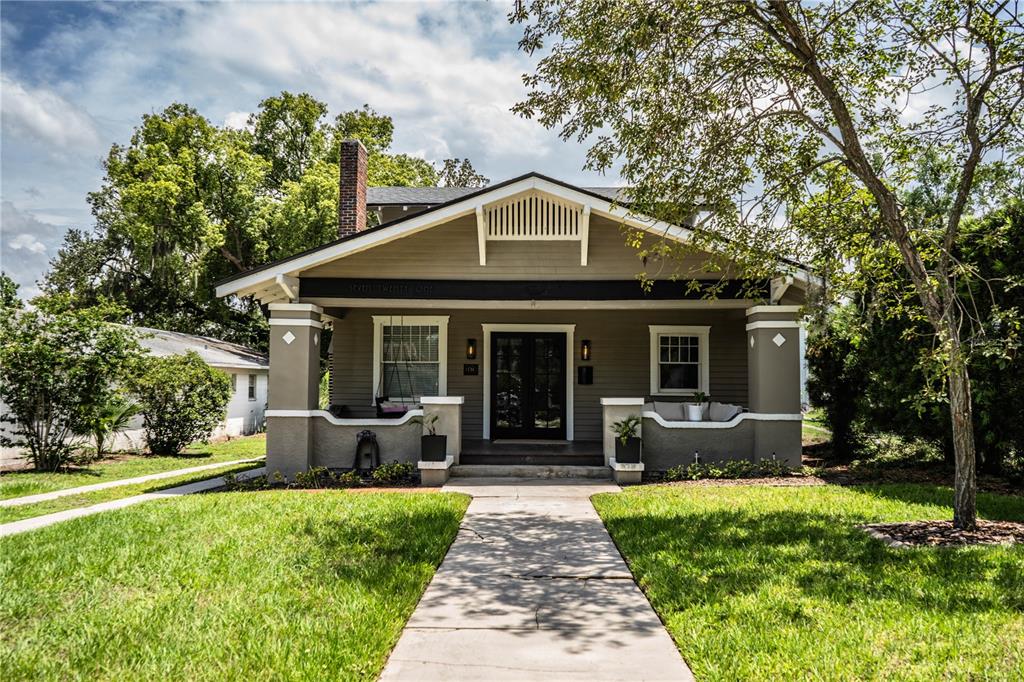 A single-story bungalow with a covered front porch, gray siding, and a brick chimney — 721 FRANK LLOYD WRIGHT WAY, LAKELAND, FL