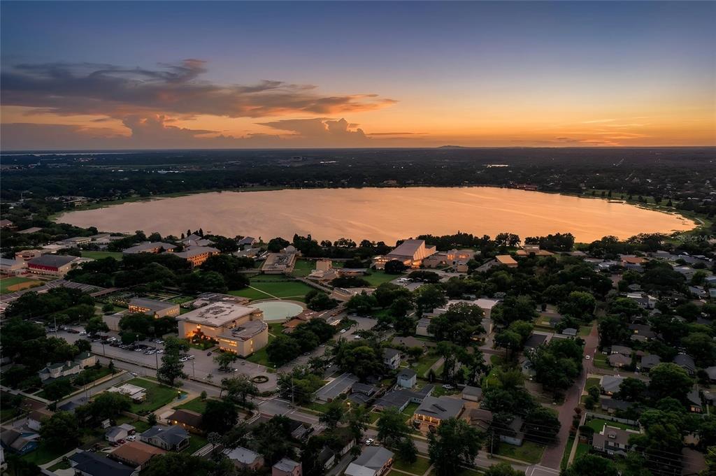 An aerial view shows a large lake at sunset behind a suburban neighborhood and campus — 721 FRANK LLOYD WRIGHT WAY, LAKELAND, FL
