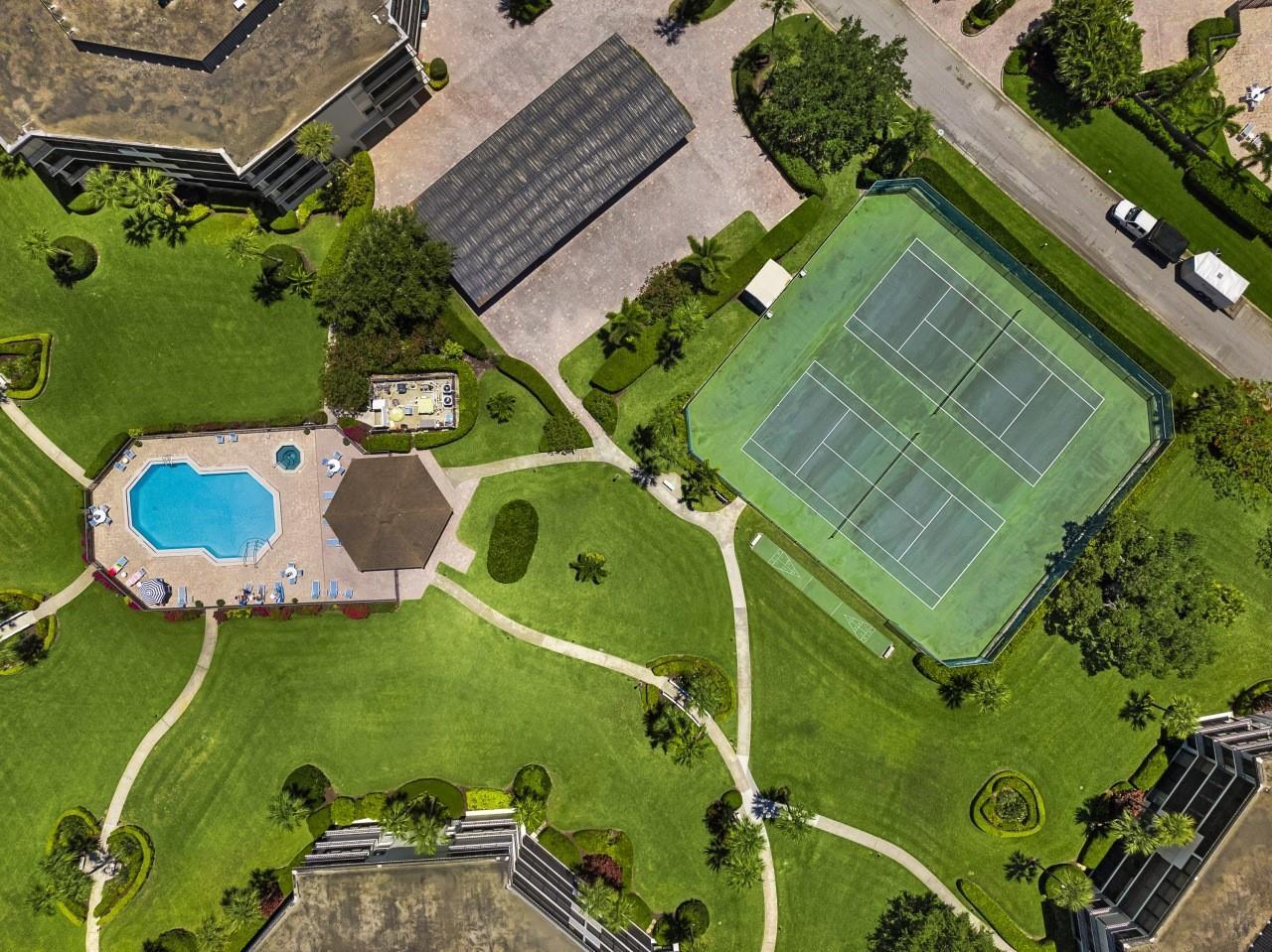 An aerial view shows a swimming pool, tennis court, and apartment buildings surrounded by landscaping — 1815 Mooringline Drive # 2e, Vero Beach FL 32963, VERO BEACH, FL