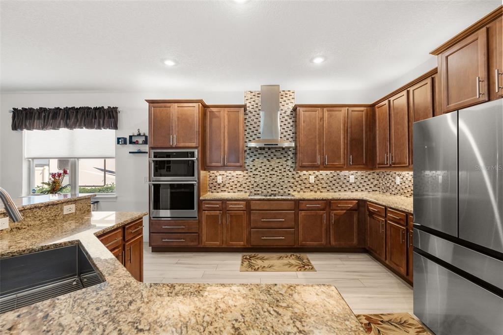 A kitchen features wood cabinets, granite countertops, stainless steel appliances, and a mosaic tile backsplash — 700 S FLORIDA AVENUE, HOWEY IN THE HILLS, FL