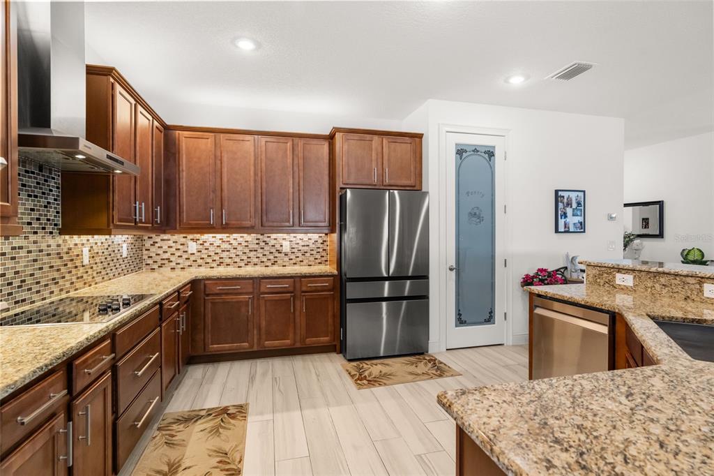 A kitchen features wood cabinets, granite countertops, stainless steel appliances, and a pantry door — 700 S FLORIDA AVENUE, HOWEY IN THE HILLS, FL