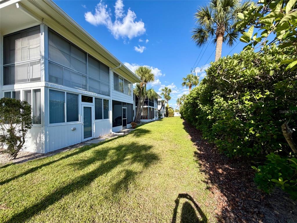 A grassy yard runs alongside a white two-story building with screened-in porches and palm trees — 3900 ROXANE BOULEVARD UNIT 11B, SARASOTA, FL