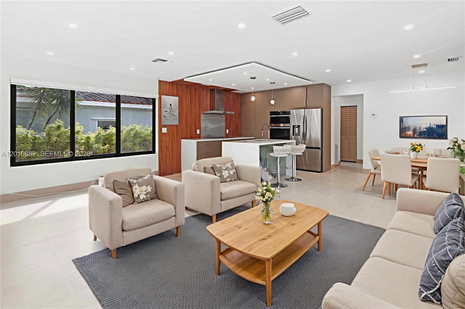 An open-concept living and dining area features a modern kitchen with wood-slat wall accents — 1620 Mckinley St, Hollywood FL 33020, HOLLYWOOD, FL