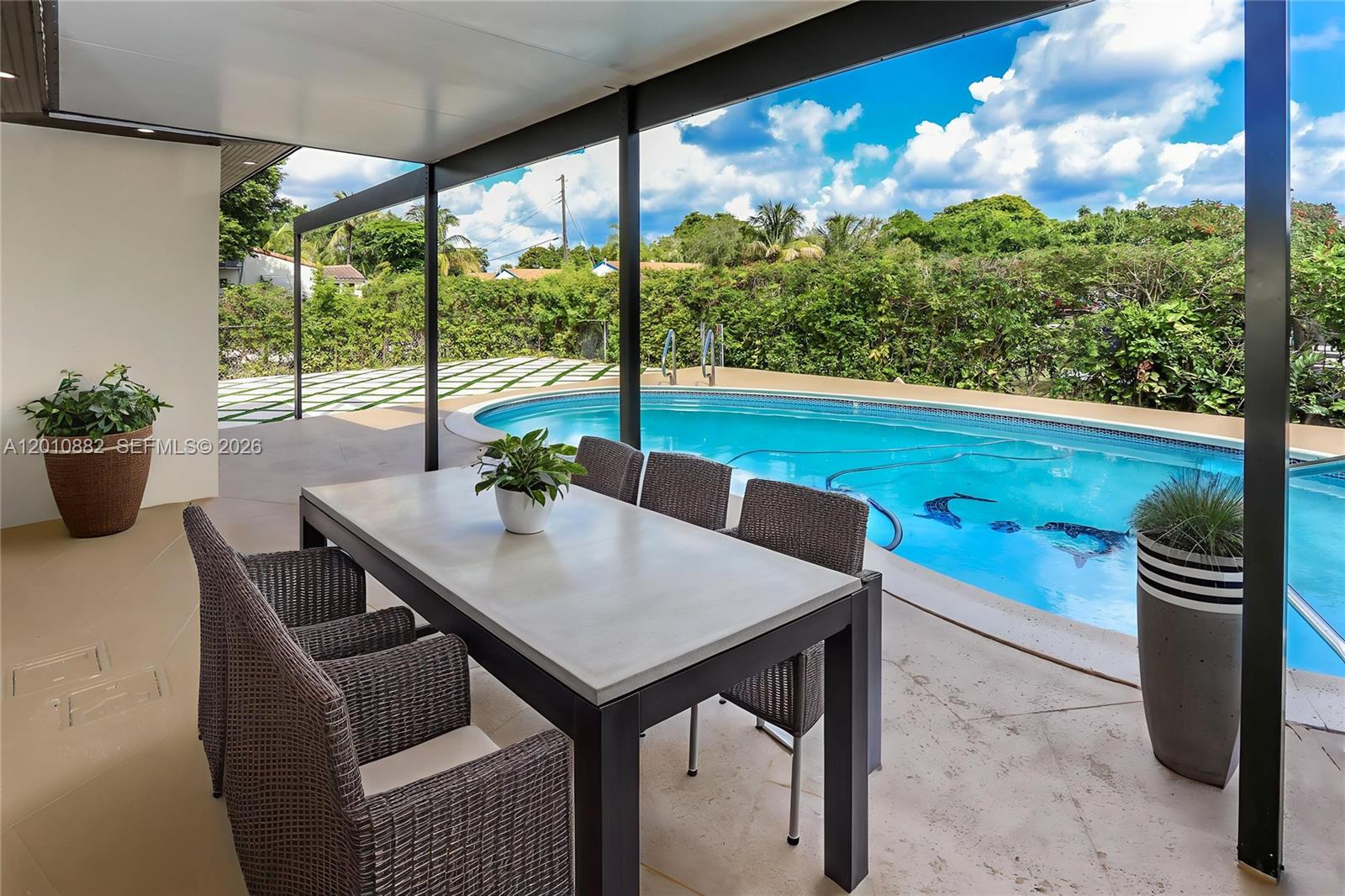 A covered patio features a dining set overlooking a swimming pool and landscaped backyard — 1620 Mckinley St, Hollywood FL 33020, HOLLYWOOD, FL