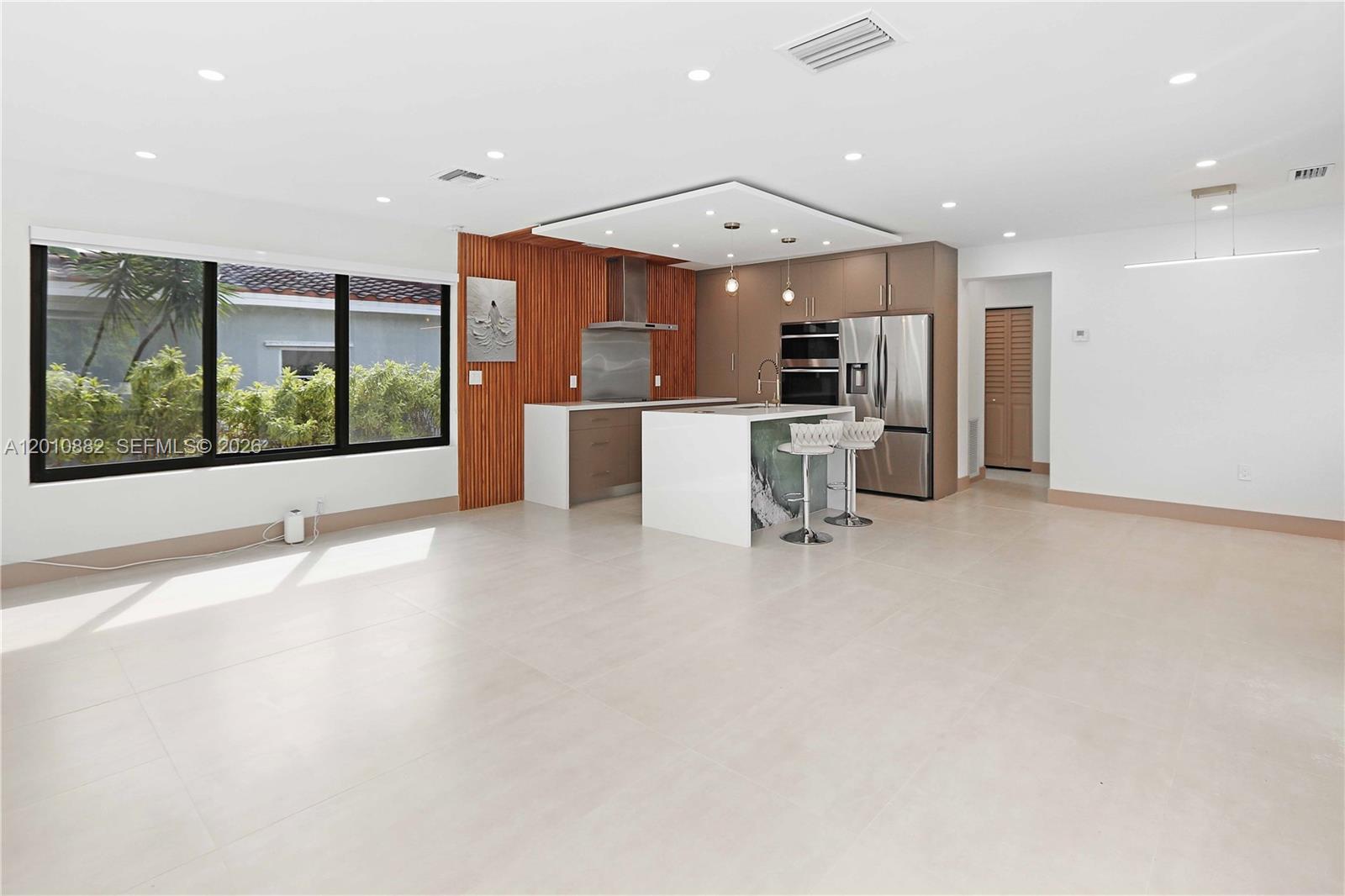 A modern kitchen features a white island, wood-slat wall, and large windows in an open space — 1620 Mckinley St, Hollywood FL 33020, HOLLYWOOD, FL