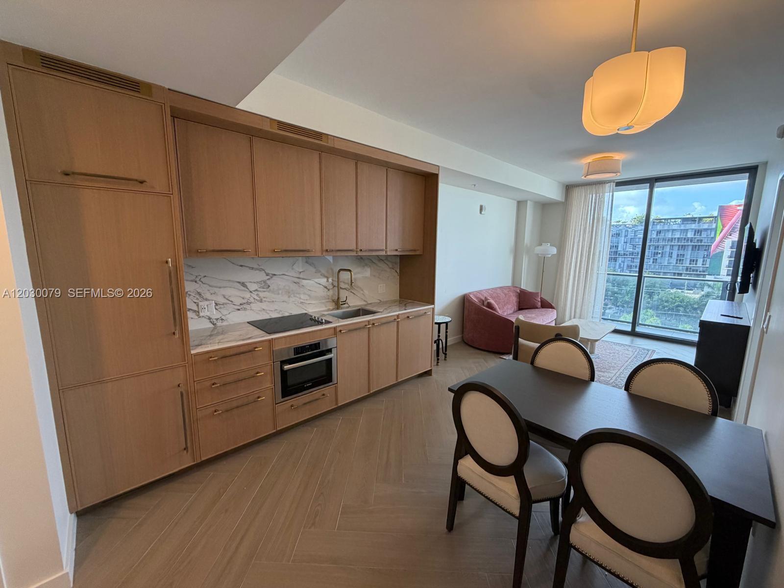 A modern kitchen with light wood cabinetry and marble backsplash opens into a dining area — 2700 NW 2nd Ave # 606, Miami FL 33127, MIAMI, FL