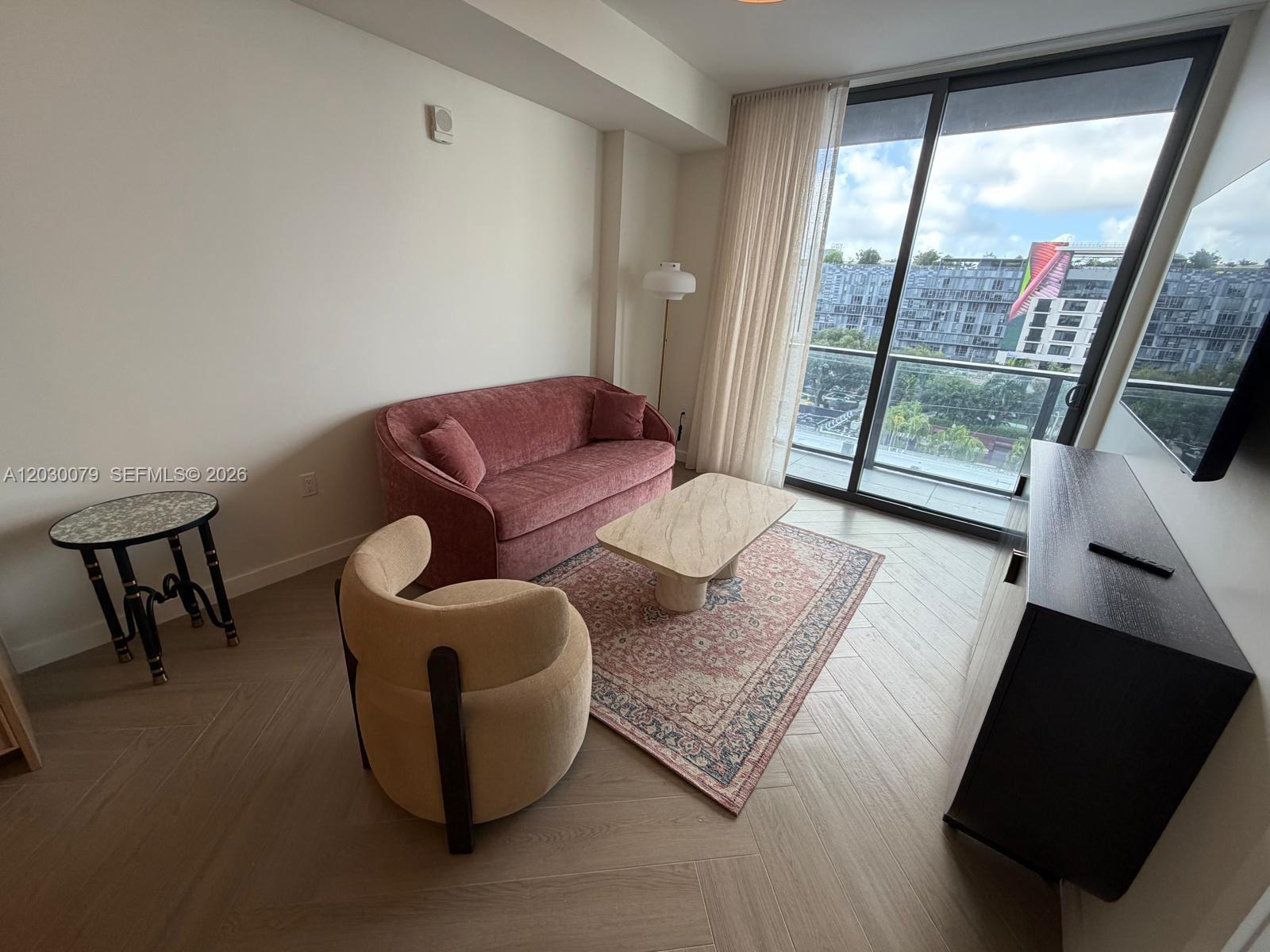 A living room features a pink sofa, a beige armchair, and a balcony with city views — 2700 NW 2nd Ave # 606, Miami FL 33127, MIAMI, FL