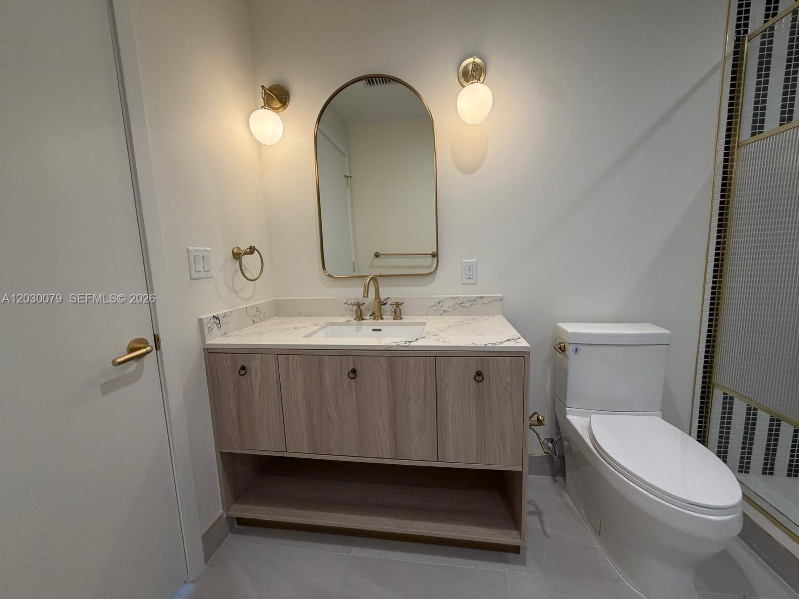 A bathroom features a light wood vanity, marble countertop, arched mirror, and gold fixtures — 2700 NW 2nd Ave # 606, Miami FL 33127, MIAMI, FL