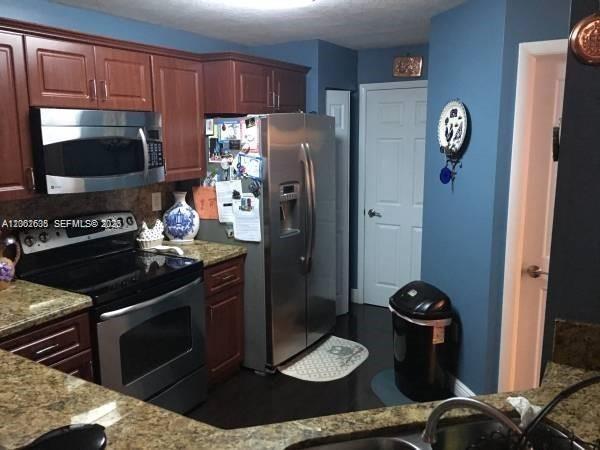 A kitchen features stainless steel appliances, wood cabinets, granite countertops, and blue walls — 8067 NW 199th Ter, Hialeah FL 33015, HIALEAH, FL