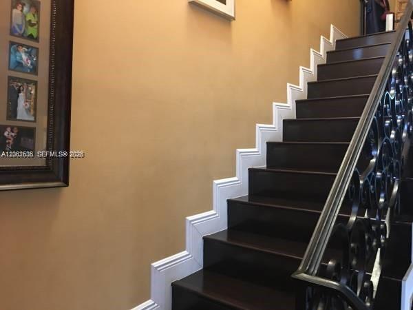 A staircase with dark wood treads and a decorative black metal railing against a wall — 8067 NW 199th Ter, Hialeah FL 33015, HIALEAH, FL