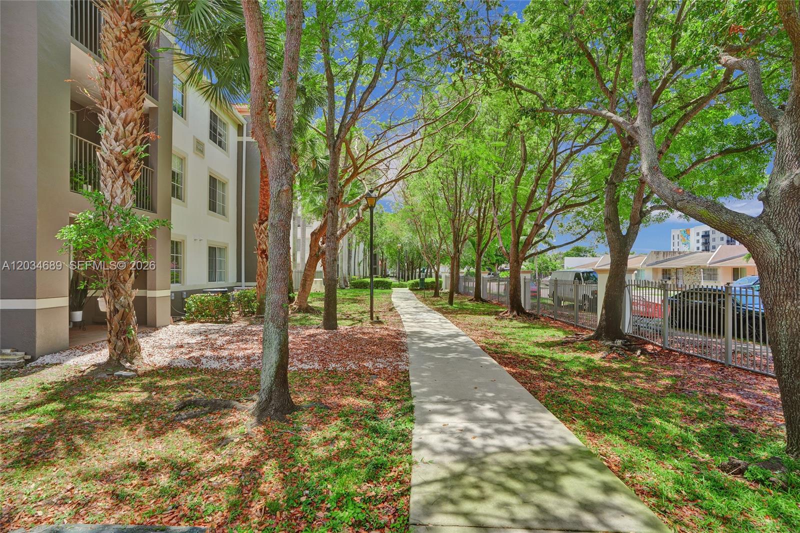 A sidewalk runs between a multi-story apartment building and a metal fence lined with trees — 6841 SW 44th St # 305, Miami FL 33155, MIAMI, FL