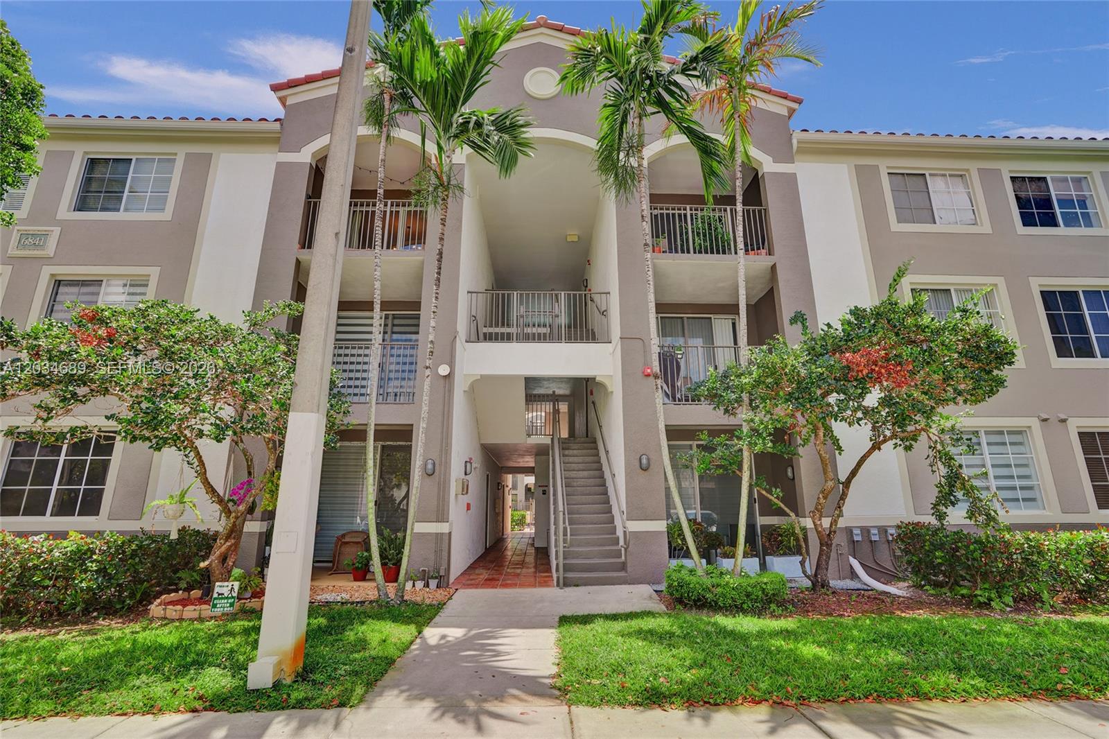A three-story apartment building exterior features a central staircase, balconies, and palm trees — 6841 SW 44th St # 305, Miami FL 33155, MIAMI, FL