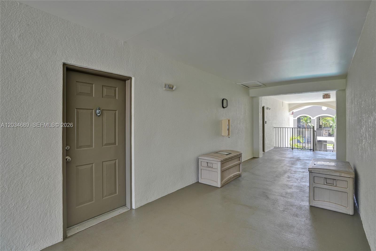 An outdoor apartment hallway features a brown door, two storage bins, and a balcony view — 6841 SW 44th St # 305, Miami FL 33155, MIAMI, FL