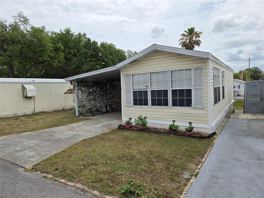 A light yellow mobile home features a carport, a front lawn, and a concrete driveway — 39326 RECESS DRIVE, ZEPHYRHILLS, FL