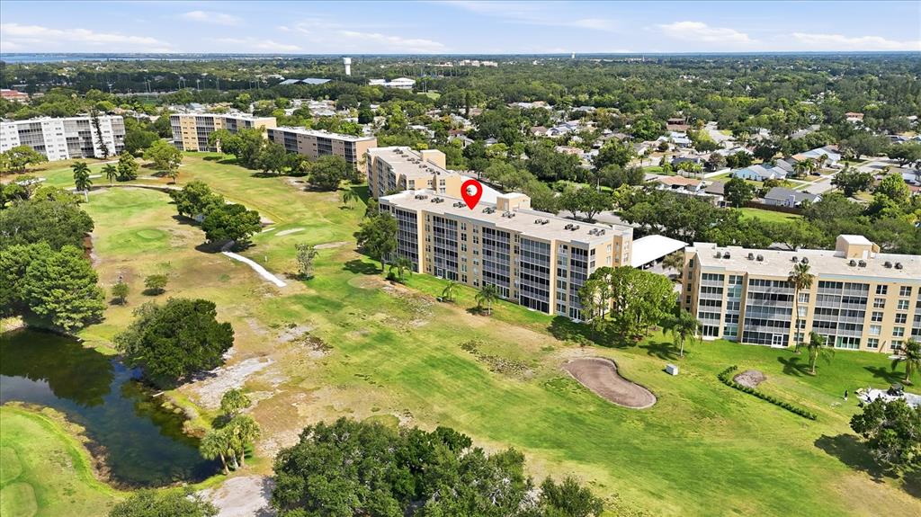 An aerial view shows multi-story apartment buildings situated alongside a golf course and pond — 3740 PINEBROOK CIRCLE UNIT 207, BRADENTON, FL