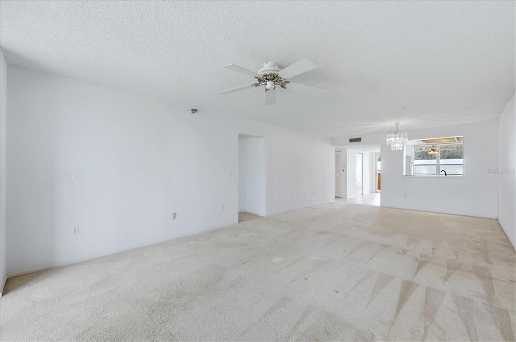 A spacious, empty living room features white walls, beige carpeting, and a ceiling fan — 3740 PINEBROOK CIRCLE UNIT 207, BRADENTON, FL