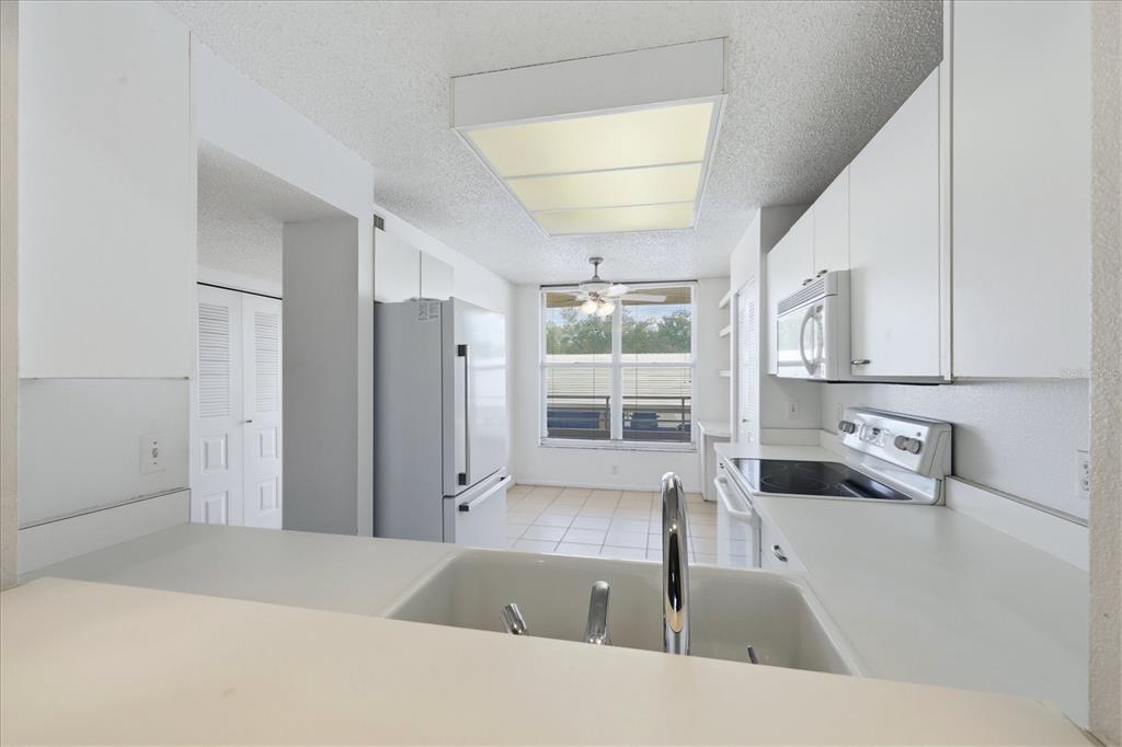 A kitchen with white cabinets, white appliances, and a window overlooking an exterior building — 3740 PINEBROOK CIRCLE UNIT 207, BRADENTON, FL