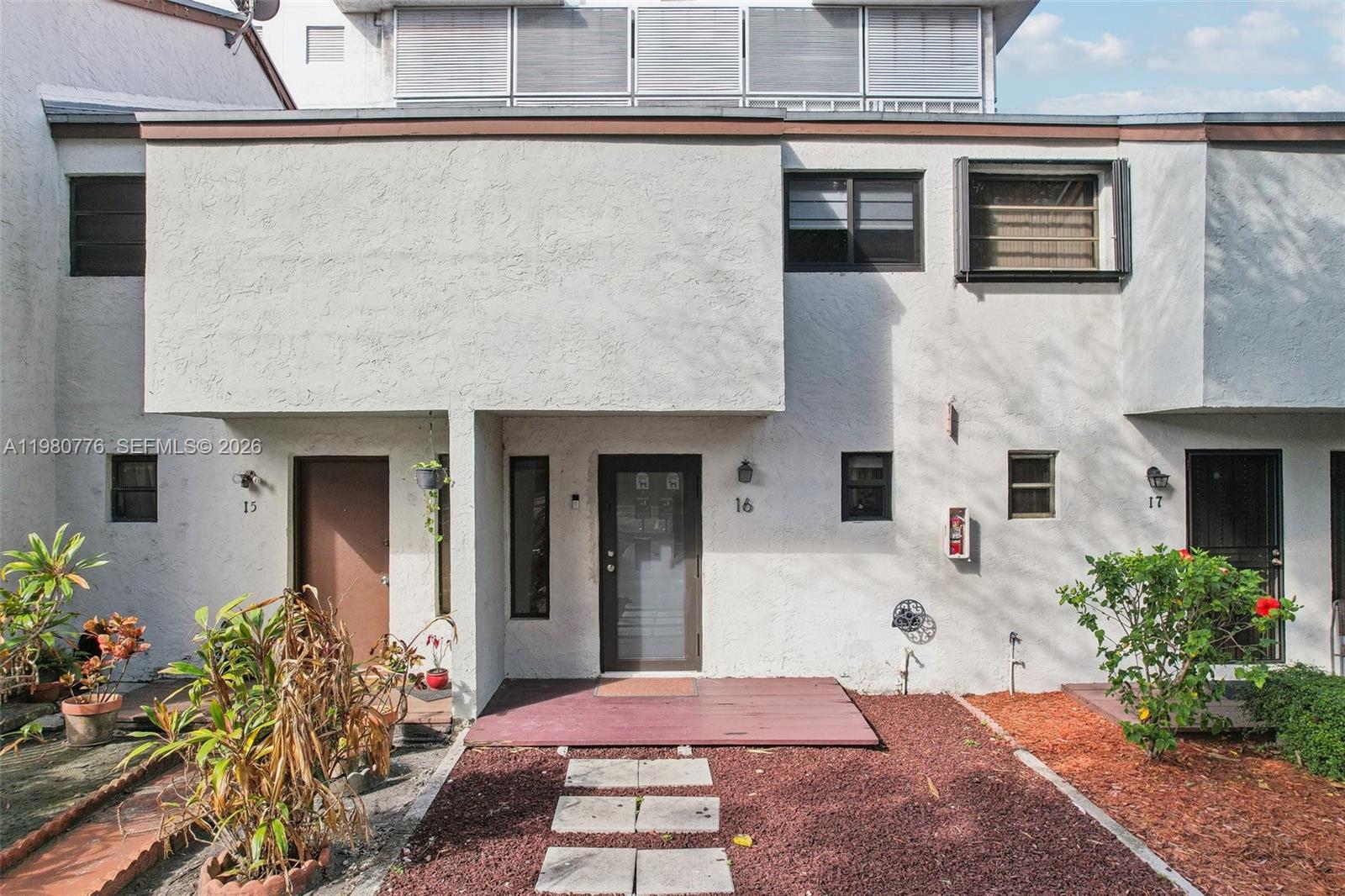The exterior of a multi-unit residential building features stucco walls, a wooden deck, and landscaping — 1901 NW S River Dr # 16B, Miami FL 33125, MIAMI, FL